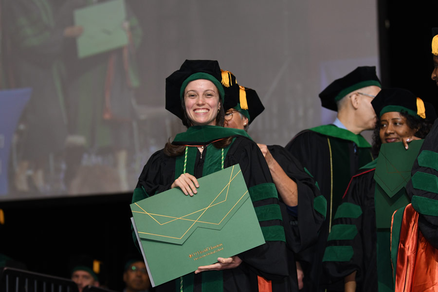 A graduate poses with a diploma cover after crossing the stage during the McGovern Medical School Class of 2026 Commencement Ceremony.