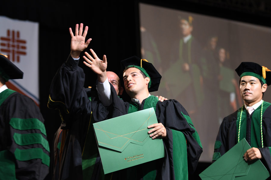 A graduate waves to family and friends while crossing the stage during commencement ceremonies.