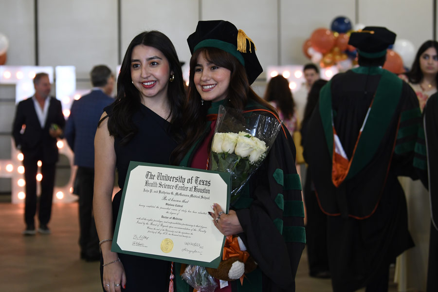 A graduate poses for a photo with a family member while holding a diploma following commencement ceremonies.