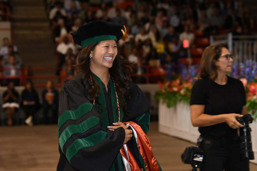 A graduate smiles while walking across the commencement stage at NRG Arena.