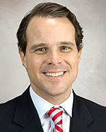 Dr. Mark Dannenbaum in a staged portrait photo with a black suit and red and white striped tie