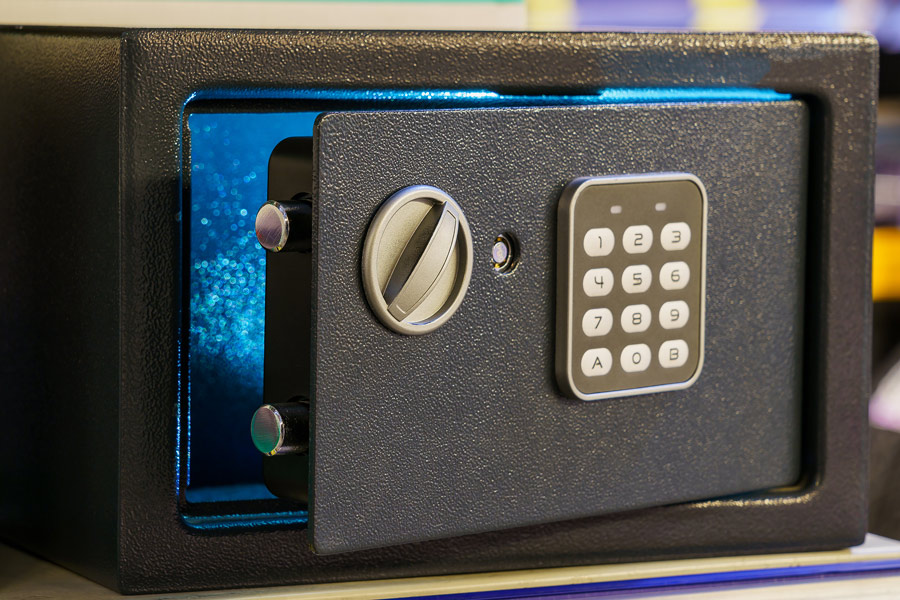 A black safe with a keypad and a dial for opening the door. The door is ajar with a blue light emitting from it.