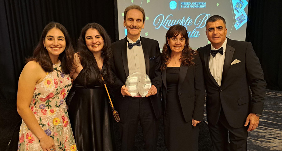 Jacques Morcos, MD, poses with the Proestakis family while holding the Patient Choice Award at the Joe Niekro Foundation Knuckle Ball Gala. The group stands together in formal attire in front of a stage backdrop displaying the event logo.