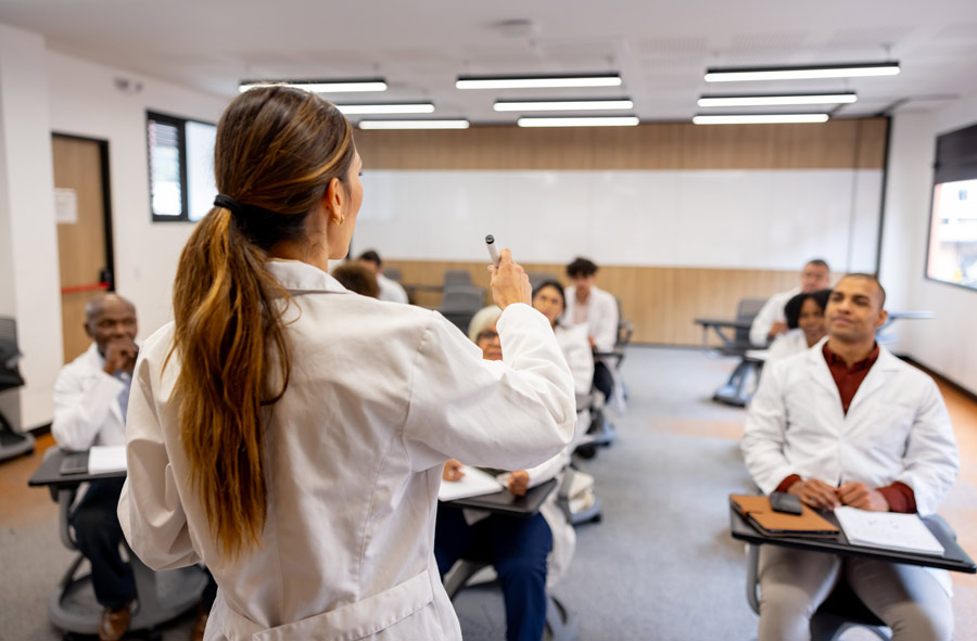 A doctor teaches a group of medical school students all dressed in their traditional white coats