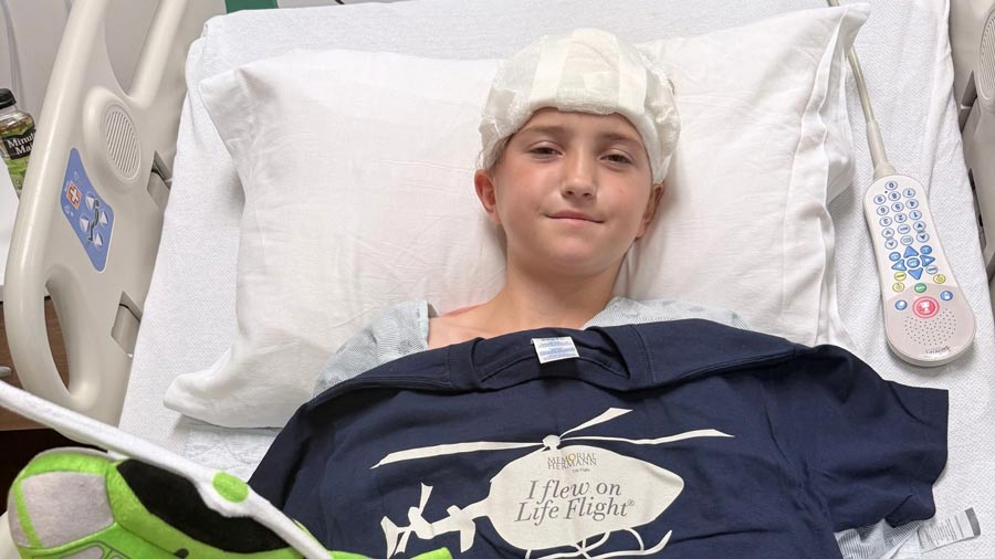 A patient recovers in a hospital bed with a bandage on their head and a blue t-shirt with a helicopter after suffering a scooter injury