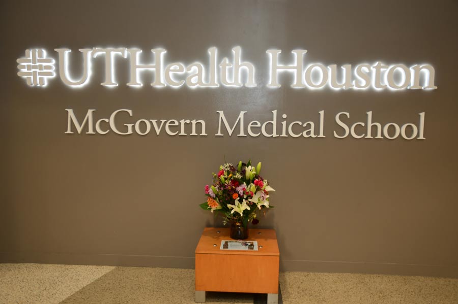 Memorial floral arrangement displayed beneath the illuminated UTHealth Houston McGovern Medical School sign in recognition of those lost during Tropical Storm Allison.
