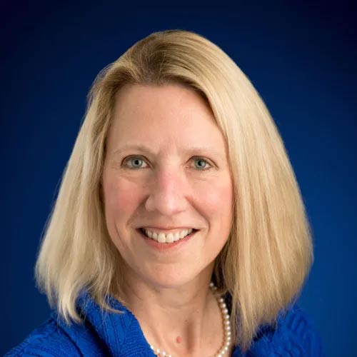 Dr. Diane Harper poses for a professional headshot in a blue shirt in front of a blue background