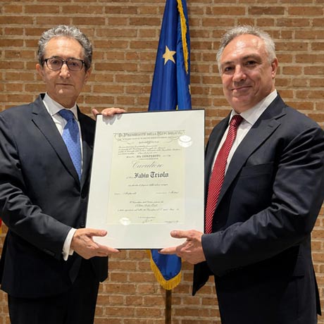 Dr. Fabio Triolo receives the Knight of the Order of Merit of the Italian Republic insignia and certificate of honor from the Consul General of Italy in Houston during a formal ceremony, holding the framed recognition together.