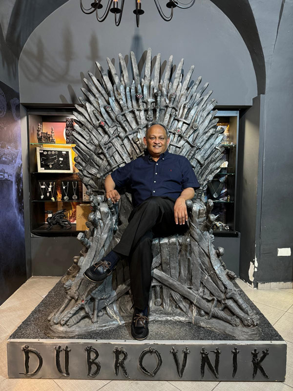 Person seated on a replica fantasy-style throne inside an exhibit space, posing for a photo.