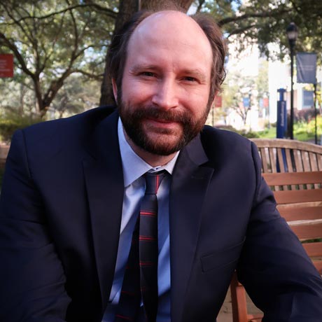 Rev. Dr. Nathan Carlin poses or a photo on a bench in a park