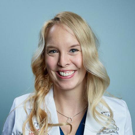 Dr. Stacey Hall poses for a professional headshot in her traditional white coat in front of a blue backgroun