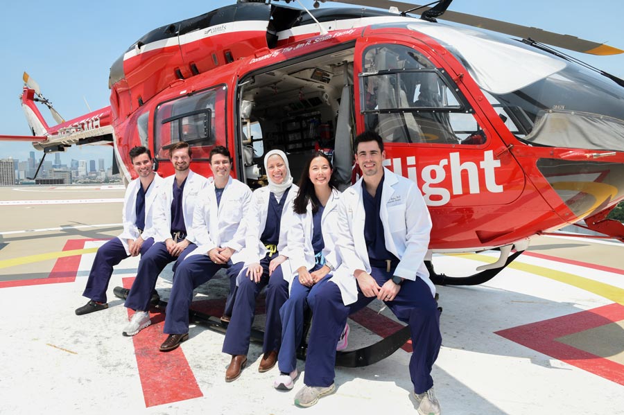 Six chief residents from the Department of Orthopedic Surgery at McGovern Medical School at UTHealth Houston pose in front of the Memorial Hermann Life Flight helicopter on the hospital's rooftop helipad, wearing white coats over navy scrubs with the Houston skyline visible in the background.