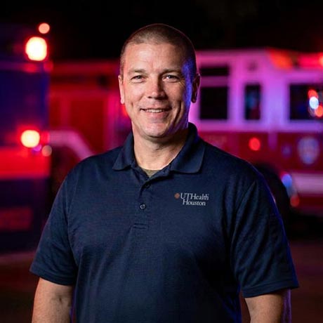 Dr. Kevin Schulz stands in front of a pair of Houston emergency vehicles at night