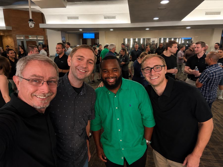 Four colleagues smile for a group selfie during a social gathering at a Nashville recording event, with attendees mingling in the background.
