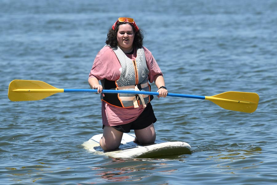 McGovern Medical School student kneels on a paddleboard while holding a double-bladed paddle on the lake.