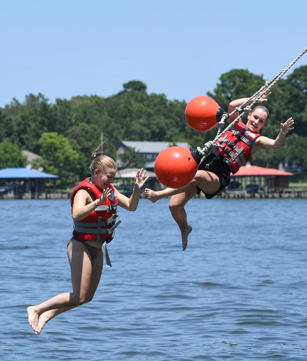 Two McGovern Medical School students wearing life jackets swing from ropes over the lake during the Henry W. Strobel Retreat.