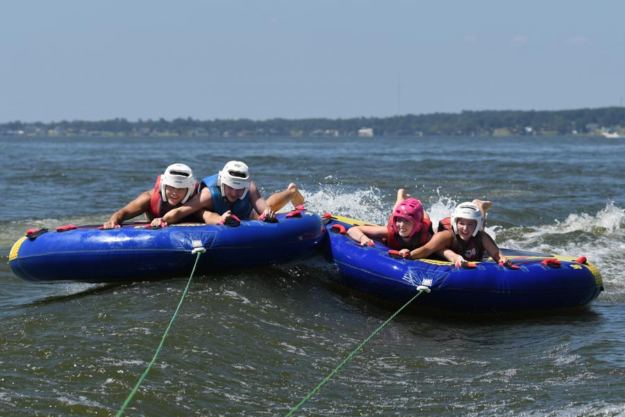 Four McGovern Medical School students ride side by side on two inflatable tubes being pulled across the lake.