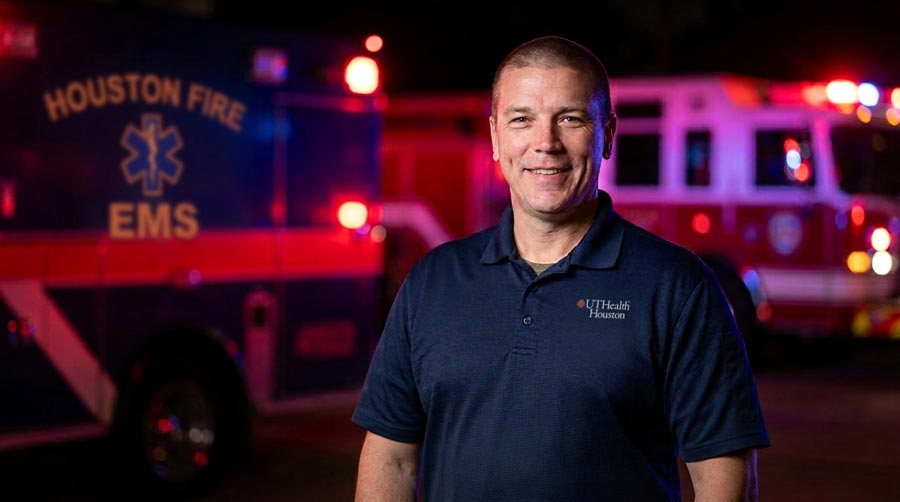 Dr. Kevin Schulz stands in front of a pair of Houston emergency vehicles at night