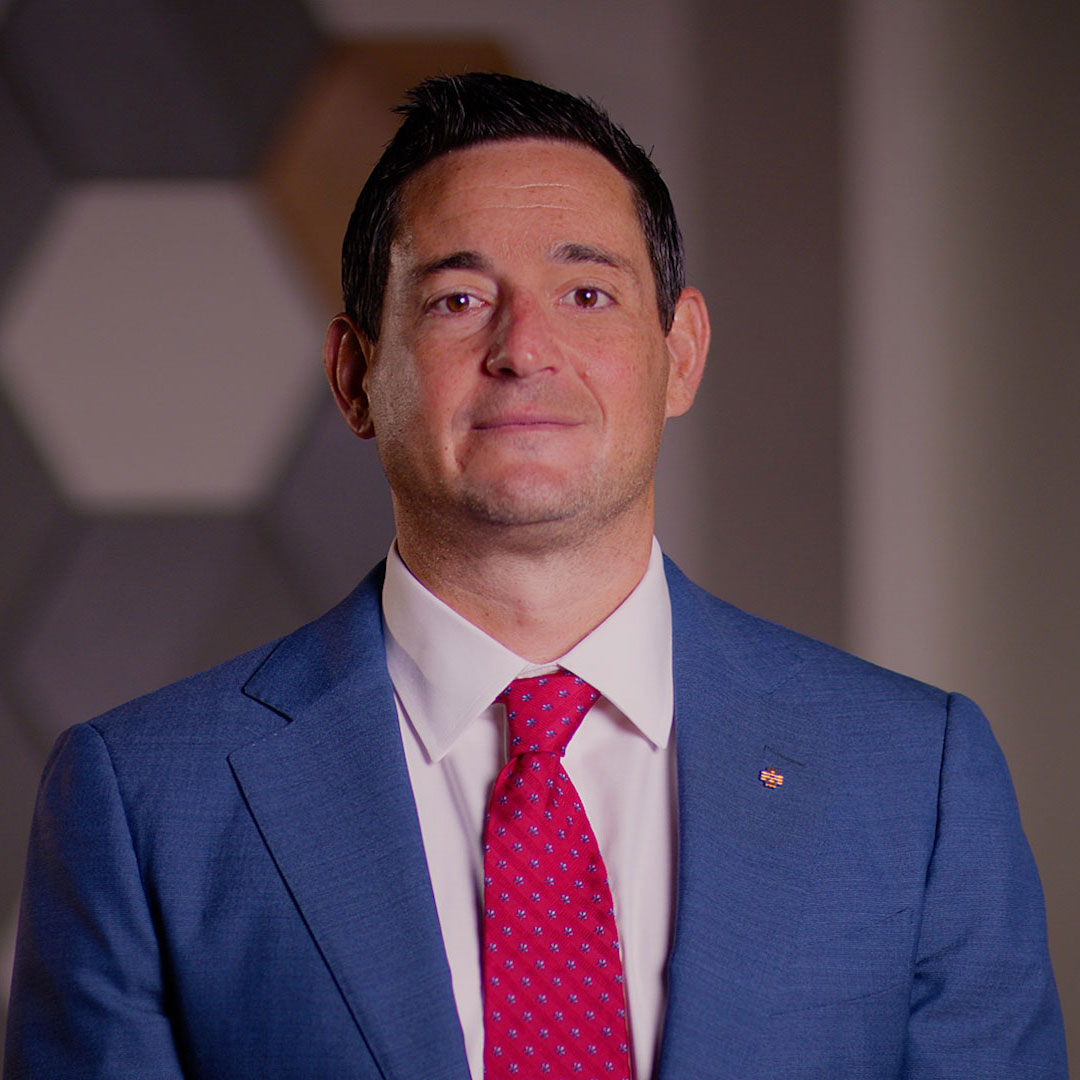 Mike Patriarca poses for a professional headshot in a blue suit with red tie and white shirt