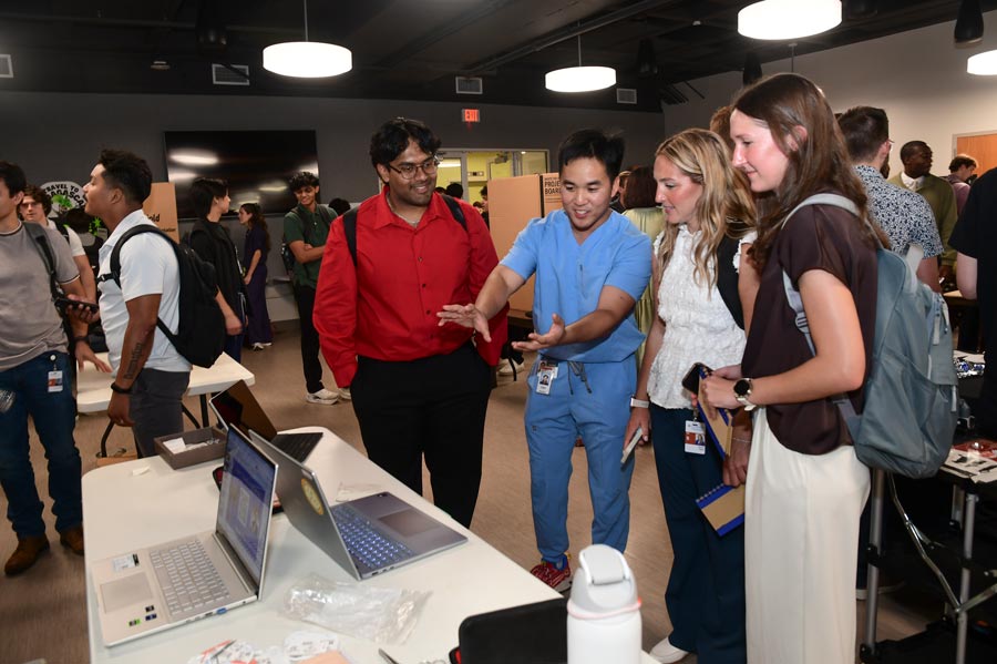 A student organization representative in scrubs demonstrates information on a laptop to students attending the Student Organization Fair.
