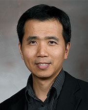 Dr. Qingchun Tong poses for a professional headshot in a black suite and black shirt in front of a gray background.