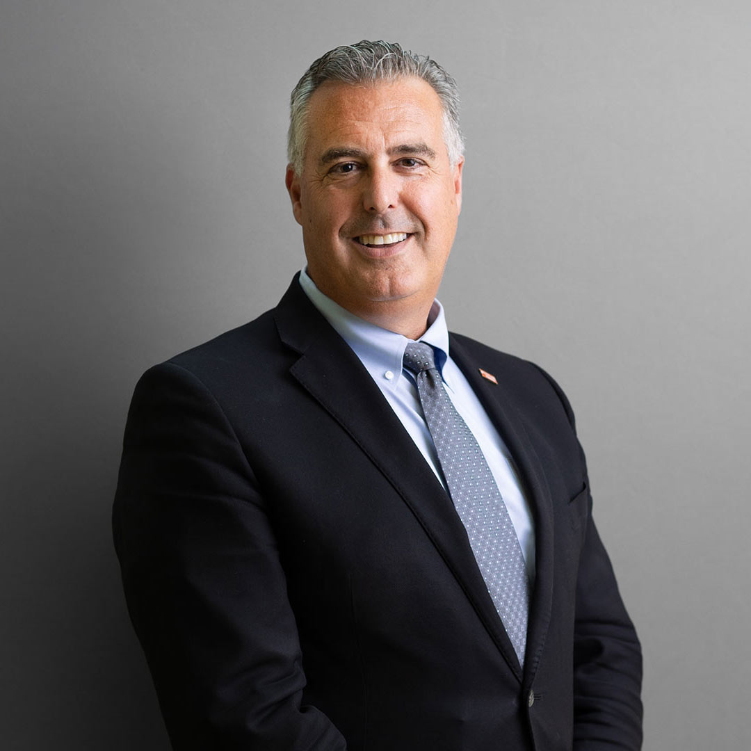 Dr. Kevin Morano poses for a professional headshot with a black suit, dark blue tie, and light blue shirt