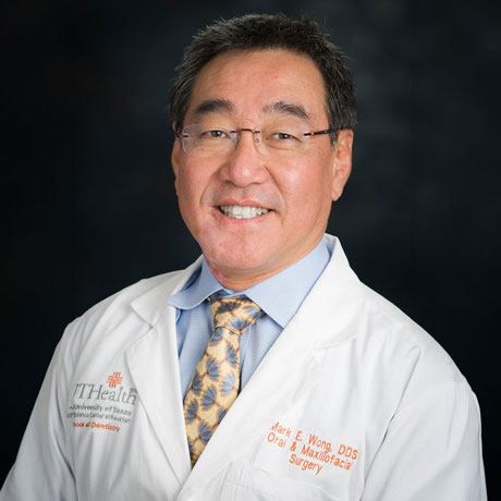 Dr. Mark Wong poses for a professional headshot in a traditional medical white coat in front of a black background