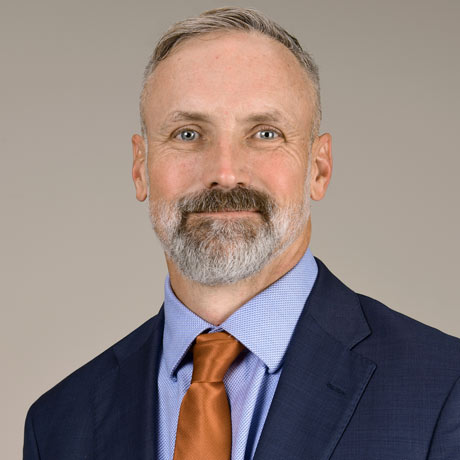 Dr. Joseph DuBose poses for a professional headshot in a dark blue suit with orange tie and blue shirt