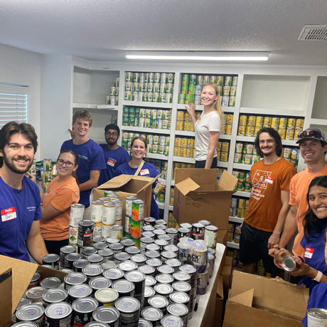 McGovern Medical School students gather around tables of canned goods while volunteering to sort and organize food donations during a PLUS service activity.