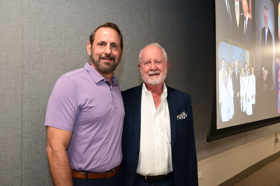 Richard Andrassy, MD, poses with a guest in front of a display featuring photos from his career.