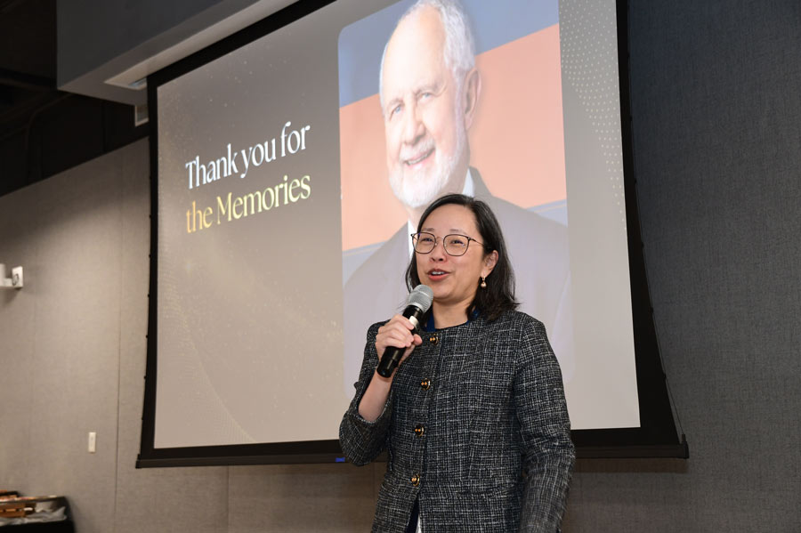 A speaker addresses guests during Richard Andrassy, MD’s retirement celebration as a tribute to Andrassy is displayed behind her.