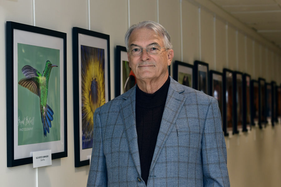 Bryant Boutwell, DrPH, stands beside a display of his framed wildlife photography.