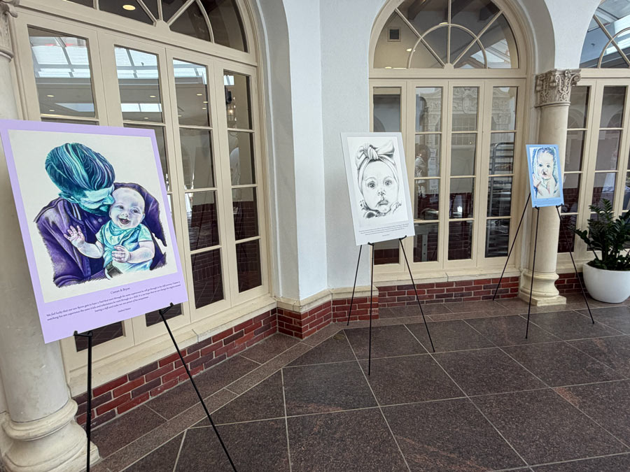 Three portraits featuring infants and their families displayed along a hallway during the 100 Cleft Portraits Tour.