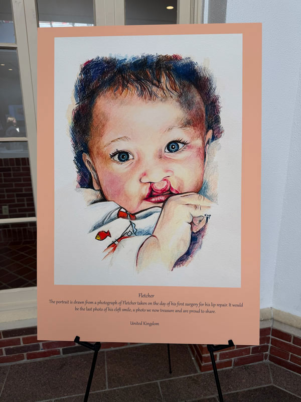 A colorful portrait of an infant named Fletcher, born with a cleft difference, displayed on an easel during the 100 Cleft Portraits Tour.