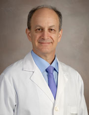 Dr. Larry Kramer poses for a professional headshot in a traditional white coat with dark blue tie and light blue shirt