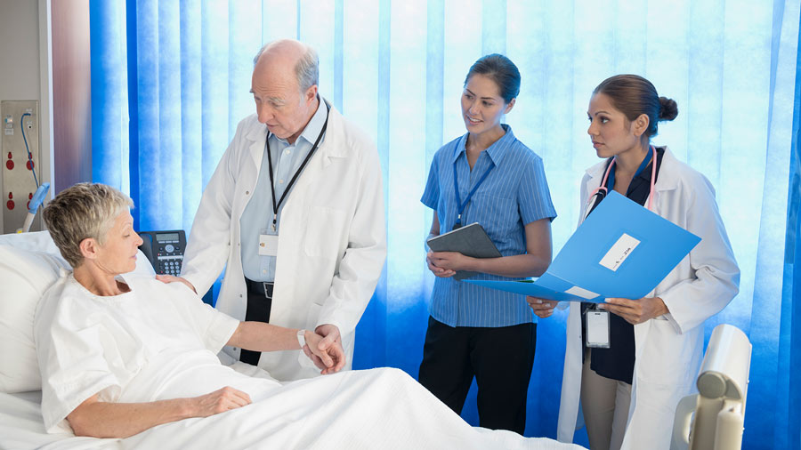 A physician and two members of a medical team visit with a patient during hospital rounds.
