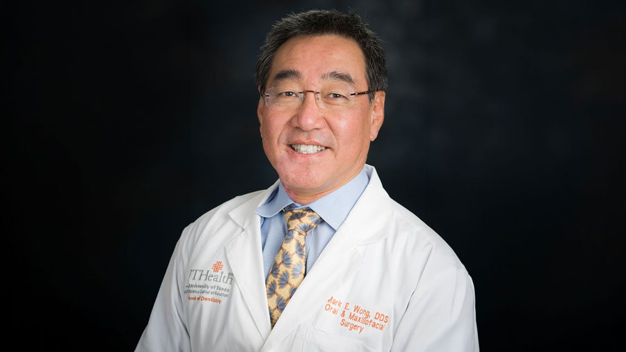 Dr. Mark Wong poses for a professional headshot in a traditional medical white coat in front of a black background
