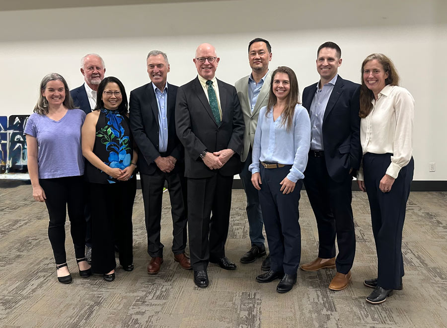 Kevin Lally, MD, MS, stands at the center of a group of nine people posing for a photograph in a conference room.