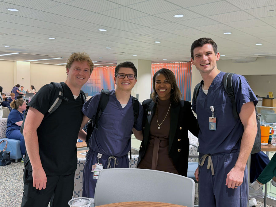 Three second-year medical students pose for a photo with a McGovern Medical School faculty leader during the MS2 pizza party.